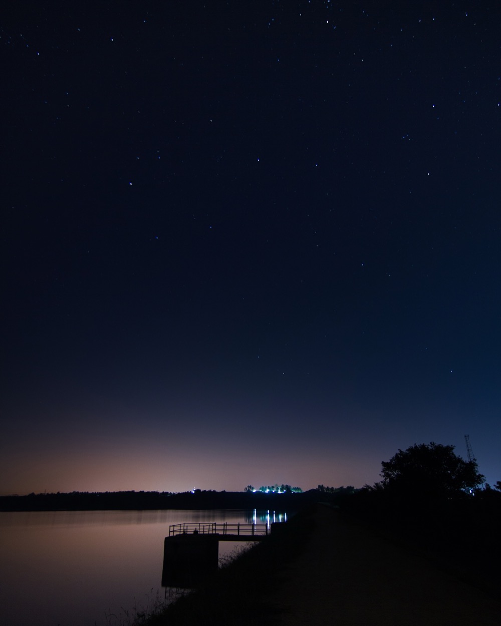 Stars over a still lake with a small jetty