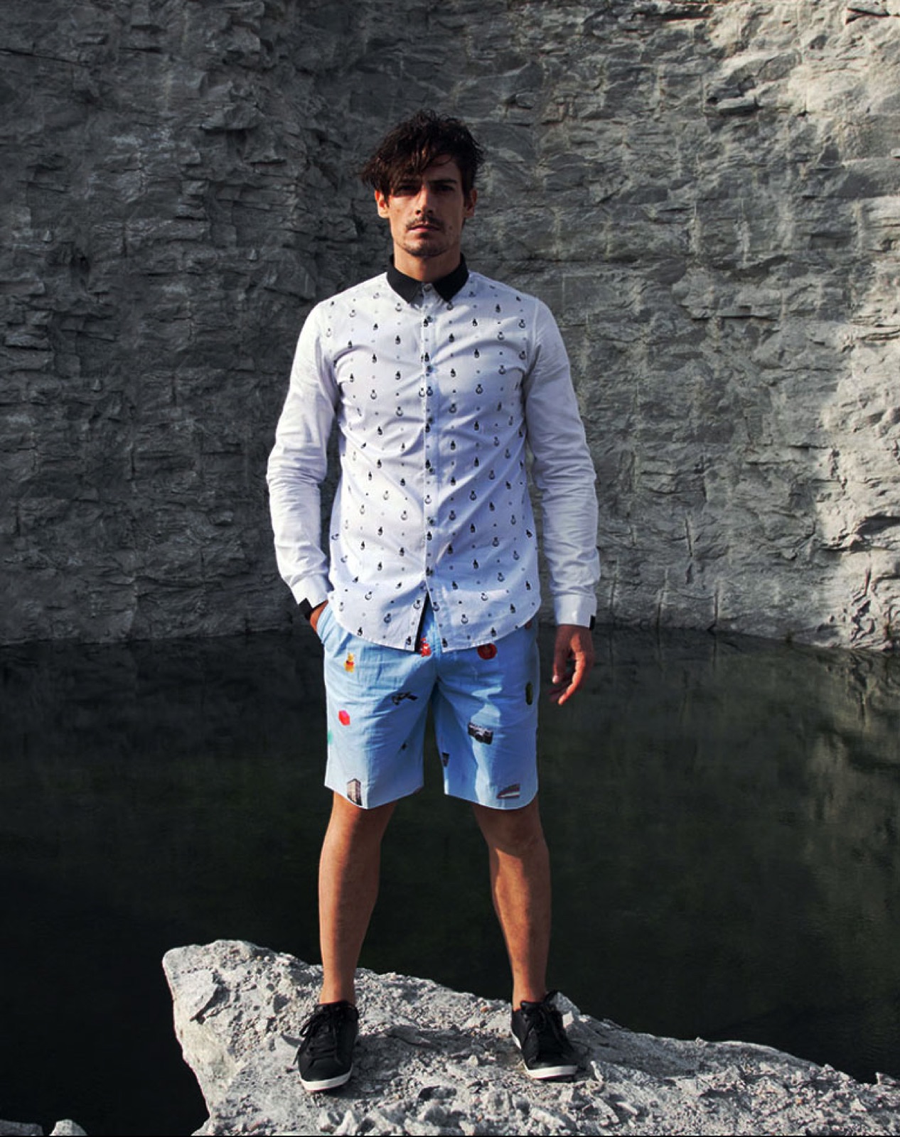 Indelust editorial photograph: a model in a white printed shirt and printed shorts standing on rock at a stone quarry, shot in natural light.